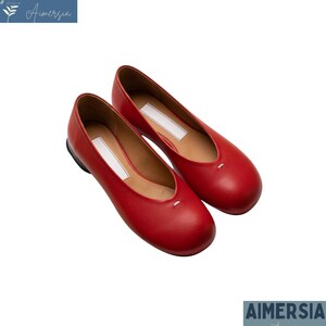 K&ouml;nnte beinhalten: Ein Paar rote Leder-Ballerinas. Die Schuhe haben eine runde Spitze und ein kleines wei&szlig;es Etikett auf der Innensohle. Die Sohle ist schwarz und das Innere hellbraun. Die Schuhe werden auf wei&szlig;em Hintergrund pr&auml;sentiert.