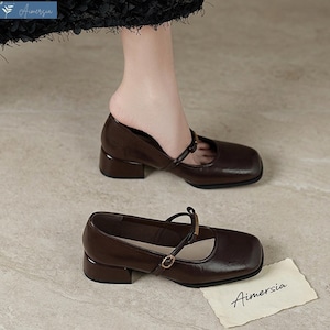 May include: Brown leather Mary Jane style shoes with a square toe and a small block heel. The shoes have a strap that fastens with a small buckle. The brand name "Aimersia" is visible on a small card.