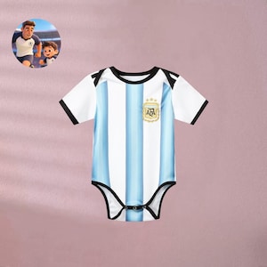 May include: A baby bodysuit featuring the Argentina national soccer team's colors: white and light blue vertical stripes. The short-sleeved onesie has black trim and a gold emblem with the letters "AFA". A cartoon image of a soccer player and a child is in the upper left corner.