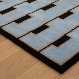 K&ouml;nnte beinhalten: Ein rechteckiger Teppich mit einem sich wiederholenden geometrischen Muster aus hellblauen, ineinandergreifenden Formen, die von d&uuml;nnen beigen R&auml;ndern auf einem einfarbigen schwarzen Hintergrund umrandet sind und ein strukturiertes Design bilden.