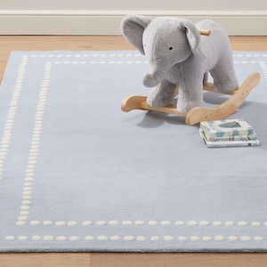 May include: A light blue area rug with a white dotted border pattern. A plush gray elephant rocker with light-colored wooden rockers sits on the rug. A small stack of three books is placed on the rug next to the elephant rocker.