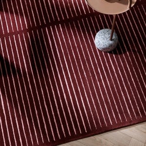May include: A burgundy rug with vertical white stripes. A small, round, brown side table with a coffee cup sits on the rug. The table has a stone base and a curved handle.