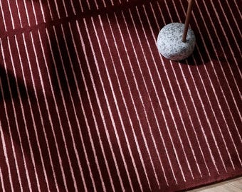 May include: A burgundy rug with vertical white stripes. A small, round, brown side table with a coffee cup sits on the rug. The table has a stone base and a curved handle.