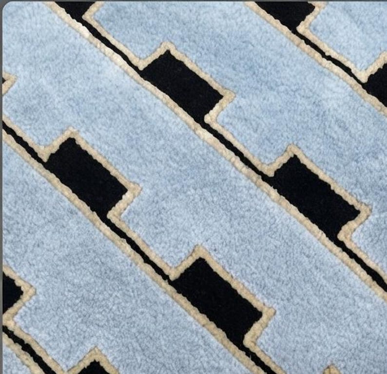 K&ouml;nnte beinhalten: Ein strukturierter Teppich mit einem sich wiederholenden geometrischen Muster aus hellblauen rechteckigen Formen, die in einer versetzten, ziegelartigen Anordnung angeordnet sind. Jeder hellblaue Bereich ist mit einem cremefarbenen Rand abgesetzt.