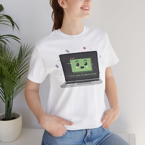 Può includere: T-shirt bianca con un design di un laptop a cartoni animati. Lo schermo del laptop è verde con una faccia sorridente e il testo "Error: object 'life_balance' not found." Piccoli elementi decorativi circondano il laptop.