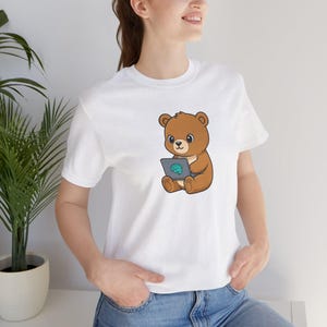 Könnte beinhalten: Weißes T-Shirt mit einem Cartoon-Bären, der einen Laptop mit einer blauen Gehirngrafik hält. Das Design ist zentriert. Das Shirt hat kurze Ärmel und einen Rundhalsausschnitt.