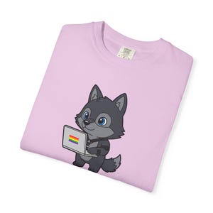Könnte beinhalten: Hellrosa T-Shirt mit einem Cartoon-Wolf, der einen Laptop mit einer Regenbogenflagge hält. Der Wolf ist grau mit blauen Augen. Das T-Shirt hat ein Comfort Colors-Etikett.