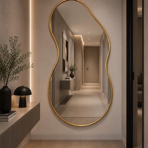 Könnte beinhalten: Ein großer Wandspiegel mit einer unregelmäßigen, organischen, amöbenartigen Form und einem dünnen, glatten, goldfarbenen Metallrahmen. Die reflektierende Oberfläche zeigt einen Flur und fängt die Tiefe und das Licht des Raumes ein.