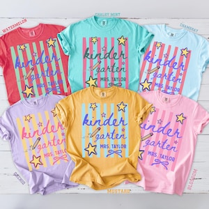 May include: Five short-sleeved t-shirts in watermelon, mint, chambray, orchid, and mustard colors. Each shirt features vertical stripes, a pencil graphic, star icons, and the text "kindergarten" with "MRS. TAYLOR" printed below in a script font.
