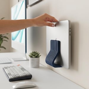 Op de afbeelding: Een donkerblauwe, geribbelde en gebogen laptopstandaard bevestigd aan de achterkant van een zilveren laptop. De standaard is voorzien van een reeks parallelle verticale ribbels en een gladde, afgeronde basis die het apparaat ondersteunt.
