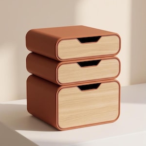 Puede incluir: Una pila de tres cajones de almacenamiento rectangulares con esquinas redondeadas. El marco exterior es de un color terracota mate sólido, mientras que cada frente de cajón presenta un acabado de veta de madera clara con un tirador recortado.