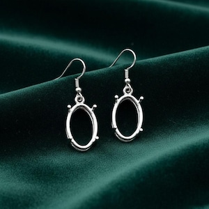 May include: A pair of silver oval earrings with hook fastenings. The earrings have a simple, elegant design. The earrings are displayed on a dark green fabric. The earrings are suitable for everyday wear.