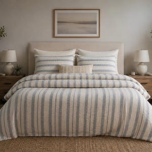 Può includere: Un set di biancheria da letto composto da un copripiumino e due federe abbinate con un motivo a righe verticali blu e bianche. Il set include un piccolo cuscino decorativo rettangolare di colore crema tinta unita al centro del letto.