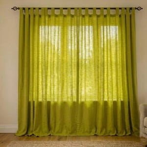 Puede incluir: Un par de cortinas de color verde lima con trabillas, hechas de una tela semitransparente y texturizada. Las cortinas cuelgan de una barra de color marrón oscuro y presentan bucles de tela espaciados uniformemente para crear pliegues.