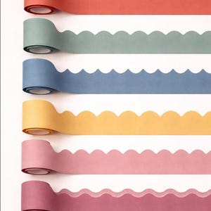 Könnte beinhalten: Sechs Rollen Papierbordüre mit gewelltem Rand, vertikal angeordnet. Die Farben von oben nach unten sind Koralle, Salbeigrün, Staubblau, Senfgelb, Hellrosa und Dunkelmalve. Jede Rolle weist ein durchgehendes, sich wiederholendes Wellenmuster auf.