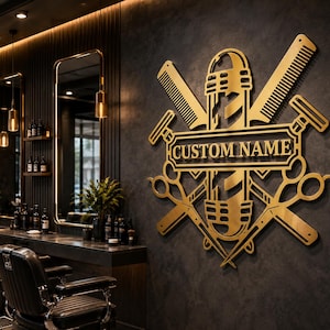 Op de afbeelding: Een goudkleurig metalen wandbord met een afbeelding van een kapperspaal gekruist met een kam, schaar en een scheermes. De centrale horizontale rechthoekige plaquette toont de tekst CUSTOM NAME in vetgedrukte hoofdletters.
