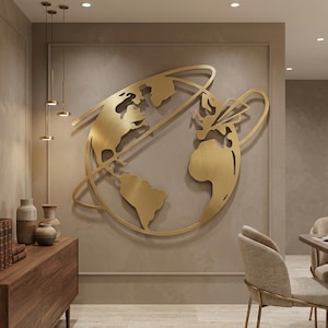 May include: A large, gold-colored metal wall art piece depicting a stylized globe with continents and orbital rings. The artwork is mounted on a neutral-toned wall, creating a striking contrast. The piece is a decorative element for interior spaces.