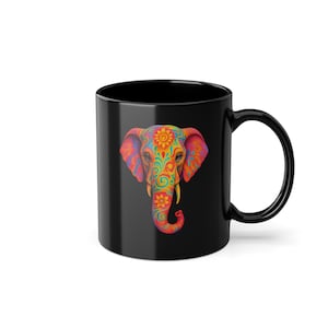 Può includere: Tazza in ceramica nera con un colorato disegno di elefante. La testa dell'elefante è decorata con motivi floreali arancioni, gialli, verdi e blu. La tazza ha un manico curvo e una finitura lucida.