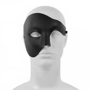 Peut inclure: Un masque noir couvrant la moitié du visage, couvrant l'œil et la joue gauches, est présenté sur une tête de mannequin blanche. Le masque est fait d'un matériau lisse et solide et est fixé avec une fine sangle noire. Accessoire théâtral.