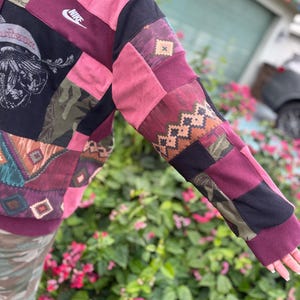 May include: A patchwork hoodie with a Nike logo. The sleeves and body are made of various fabrics in shades of burgundy, black, pink, and olive green. The design includes geometric and tribal patterns.