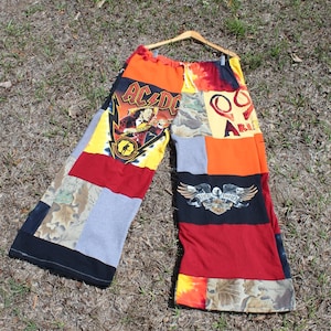 May include: Wide-leg patchwork pants featuring various fabric panels including an AC/DC graphic, a Harley-Davidson Free Bird logo, camouflage print, tie-dye, and solid red, orange, black, and gray sections with an elastic drawstring waistband.