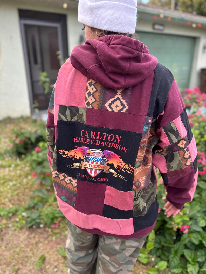 May include: A patchwork hoodie in shades of burgundy, pink, and black. The back features a Harley-Davidson logo with the text "CARLTON HARLEY-DAVIDSON AUTHENTIC MANTUA, OHIO". The hoodie has a hood and is made of various fabric patterns.