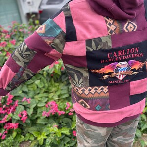 May include: A patchwork hoodie with a burgundy hood and pink body. The sleeves feature patterned fabric patches in green, burgundy, and black. The back displays a black panel with "CARLTON HARLEY-DAVIDSON" and a graphic.