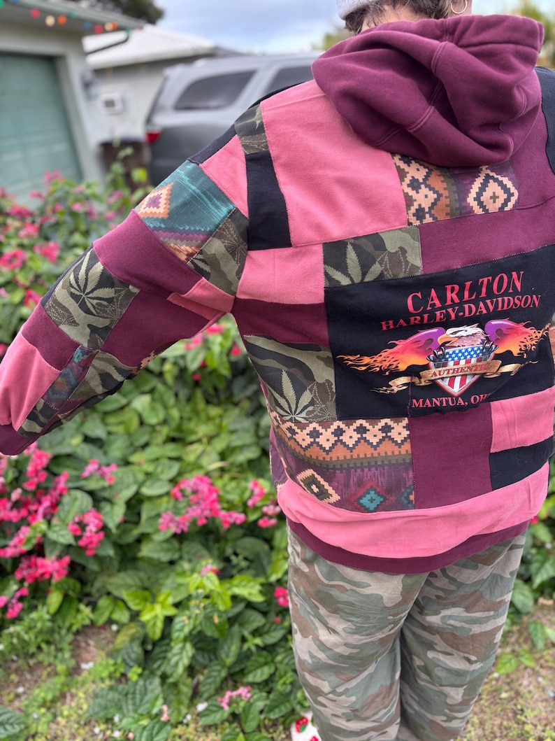 May include: A patchwork hoodie with a burgundy hood and pink body. The sleeves feature patterned fabric patches in green, burgundy, and black. The back displays a black panel with "CARLTON HARLEY-DAVIDSON" and a graphic.