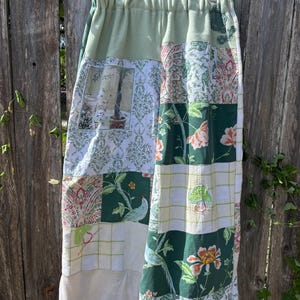 May include: A patchwork skirt featuring a variety of fabric patterns including floral prints, damask, and a bird motif in shades of green, white, and pink. The skirt has an elasticized waistband and is constructed from multiple rectangular fabric panels.