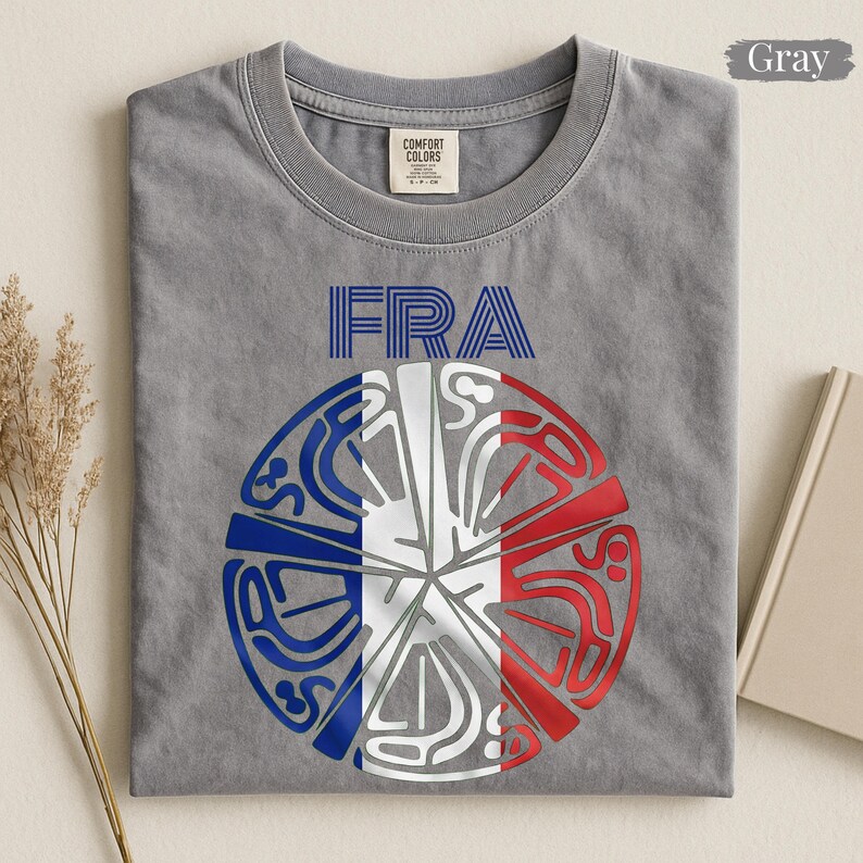 May include: A gray crew neck t-shirt featuring the text "FRA" in blue striped lettering above a circular graphic. The graphic is divided into segments colored blue, white, and red, with intricate white line art patterns overlaid throughout.