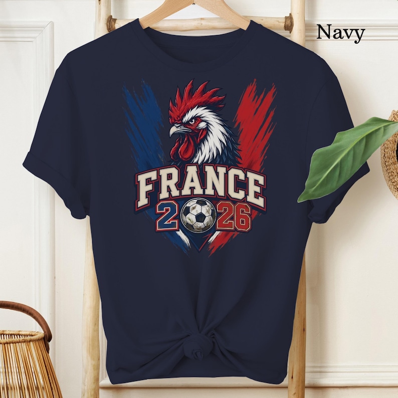 May include: Navy blue t-shirt featuring a rooster design with red, white, and blue accents, and the text "FRANCE 2026" with a soccer ball graphic. The shirt is a short-sleeved crew neck.