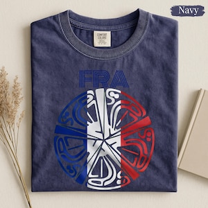 May include: A navy blue crew neck t-shirt featuring the text FRA in blue outline letters above a circular graphic. The circular design incorporates the blue, white, and red colors of the French flag with intricate, stylized, and abstract line patterns.