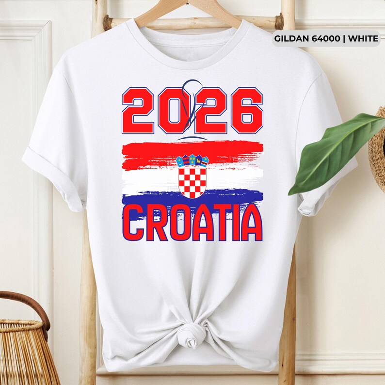 May include: White t-shirt with a graphic design featuring the text "2026" in red, above a red, white, and blue brushstroke design, and the word "CROATIA" in red. The shirt has a crew neck and short sleeves.