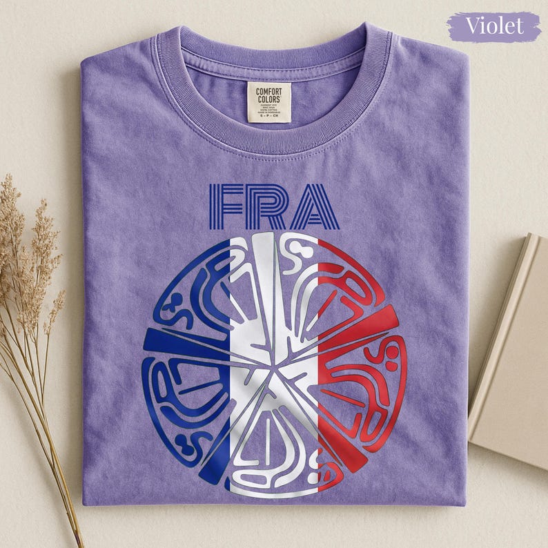 May include: A violet crew neck t-shirt featuring the text FRA in blue lines above a circular graphic. The graphic is divided into segments colored in blue, white, and red, resembling the French flag, with intricate white line art patterns.