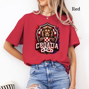 May include: Red t-shirt featuring a shield design with a lion, a checkered pattern, and the text "CROATIA 2026". The design is accented with red, white, and blue colors. The shirt is made of a soft material.