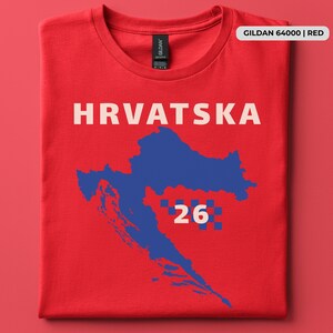 Op de afbeelding: Een rood t-shirt met korte mouwen met het woord HRVATSKA in witte hoofdletters boven een blauwe silhouetkaart van Kroati&euml;. Het ontwerp bevat een klein blauw-wit geblokt patroon naast het witte cijfer 26 op de grafische kaart.