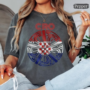 May include: A charcoal gray t-shirt featuring a circular graphic with the text CRO above it. The circular design incorporates the red, white, and blue colors of the Croatian flag with a central red and white checkerboard pattern.