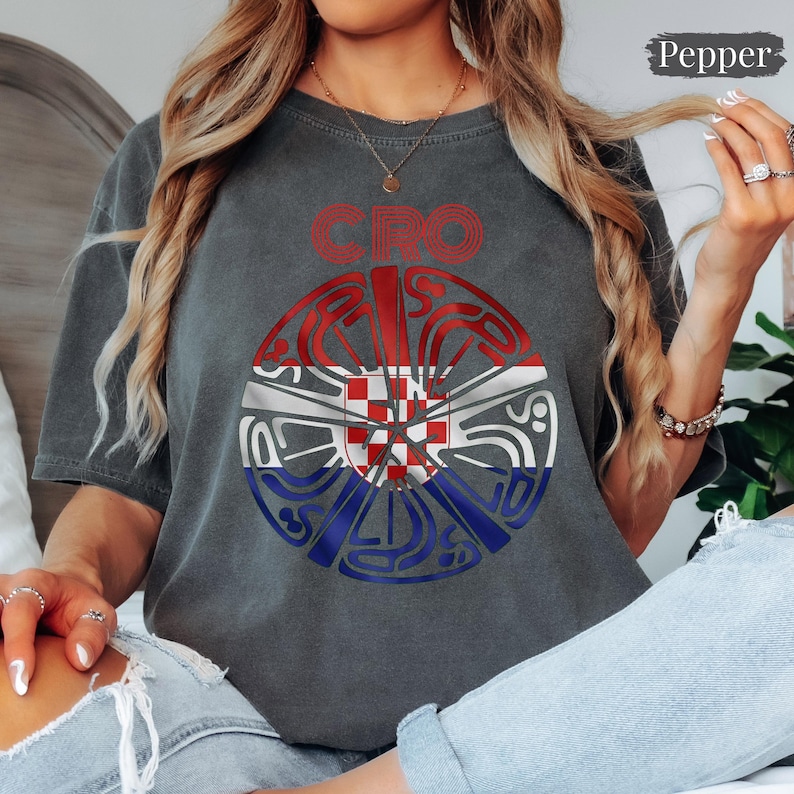 May include: A charcoal gray t-shirt featuring a circular graphic with the text CRO above it. The circular design incorporates the red, white, and blue colors of the Croatian flag with a central red and white checkerboard pattern.