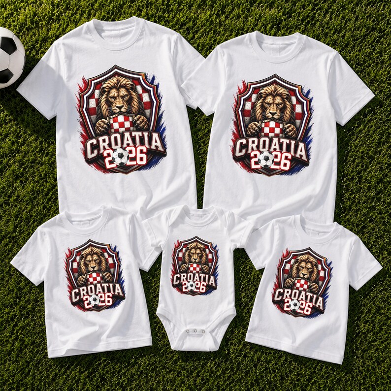 May include: White t-shirts and a onesie with a Croatia 2026 design. The design features a lion holding a soccer ball and a Croatian flag shield. The shirts are on a green grassy surface.