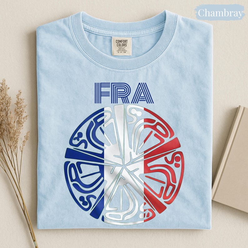 May include: A light blue t-shirt featuring the text FRA in blue above a circular graphic. The graphic displays a stylized design with white, blue, and red segments arranged in a radial pattern, resembling a fragmented French flag with intricate lines.
