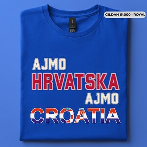 May include: A royal blue short-sleeve t-shirt featuring the text AJMO HRVATSKA AJMO CROATIA in white and red block lettering. The word CROATIA incorporates a red and white checkered pattern within its letters. A Gildan 64000 label is visible.