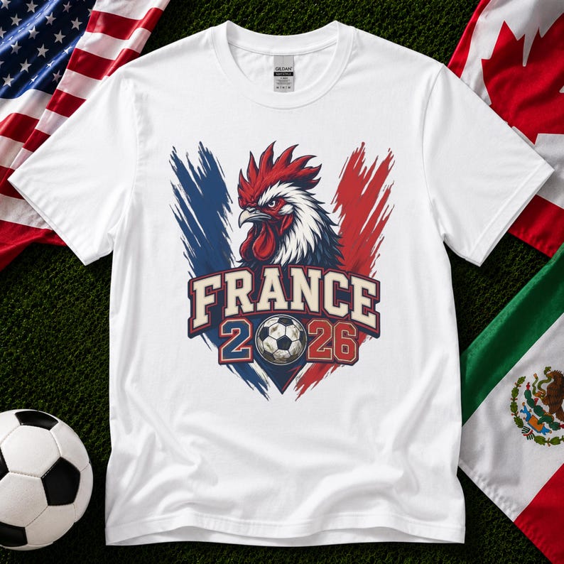 May include: White t-shirt featuring a graphic of a rooster with red, white, and blue accents, the text "FRANCE 2026", and a soccer ball. The shirt is surrounded by flags of the United States, Canada, and Mexico.