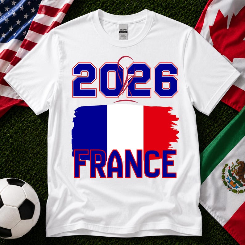 May include: White t-shirt with the text "2026 FRANCE" in blue and red, featuring the French flag design. A soccer ball and flags of the USA, Canada, and Mexico are in the background. The shirt is made of a soft material.