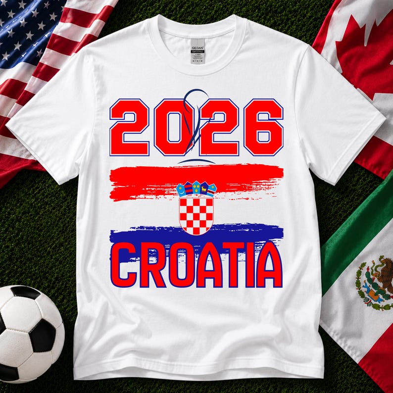 May include: White t-shirt with a red and blue design. The shirt features the number "2026" in red, above a red and blue brushstroke design, and the word "CROATIA" in red. A soccer ball and flags are in the background.