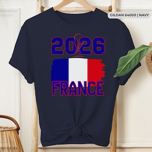 May include: Navy blue t-shirt with the text "2026 FRANCE" in red and blue, featuring the French flag. The shirt is a Gildan 64000 in navy.