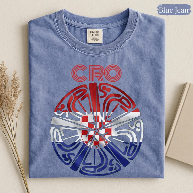 May include: A blue jean colored t-shirt with a crew neckline and a Comfort Colors label. The graphic features the red text CRO above a circular design containing the red, white, and blue Croatian flag pattern with stylized, swirling line art.