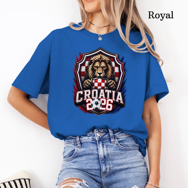 May include: Royal blue t-shirt featuring a graphic of a lion holding a Croatian checkered shield, with the text "CROATIA 2026" and a soccer ball. The design is framed by red and blue accents.