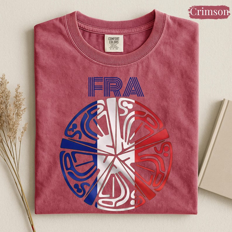 May include: A crimson short-sleeve t-shirt featuring the text FRA in blue and a circular graphic design below it. The graphic is divided into segments colored in blue, white, and red, resembling the French flag with intricate line patterns.