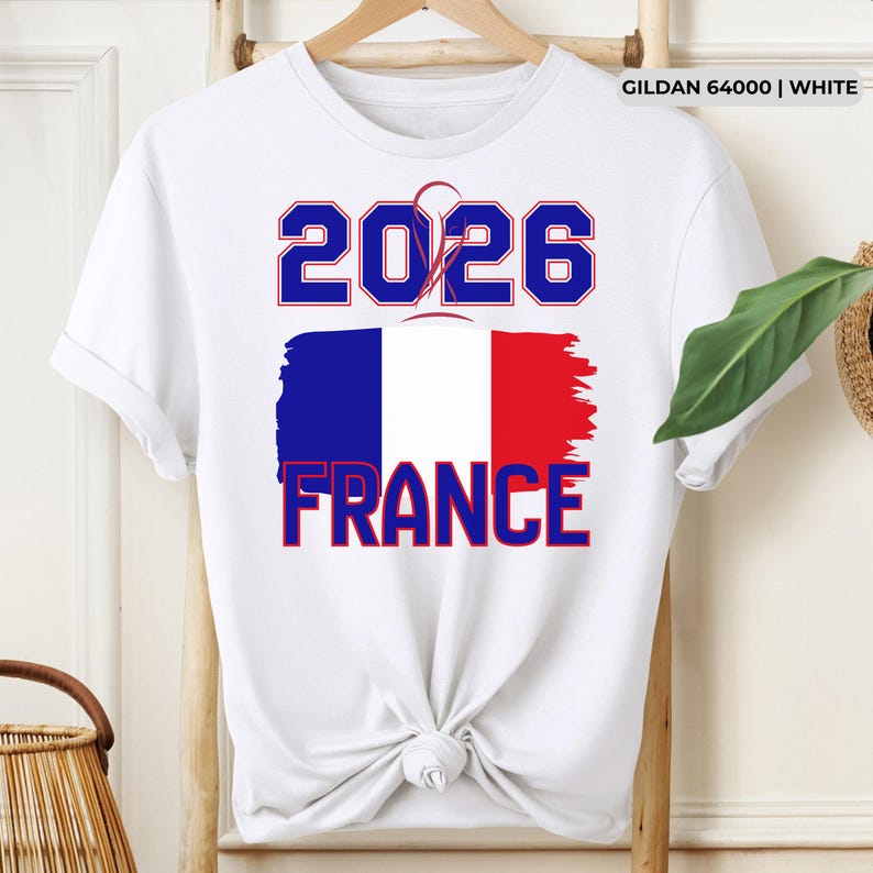May include: White t-shirt with the text "2026 FRANCE" in blue and red, featuring a stylized French flag design. The shirt is made of white fabric and has a crew neck.