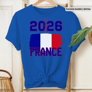May include: Royal blue t-shirt featuring the text "2026 FRANCE" in red and white, with a stylized French flag design. The shirt is made of a soft material and has short sleeves.